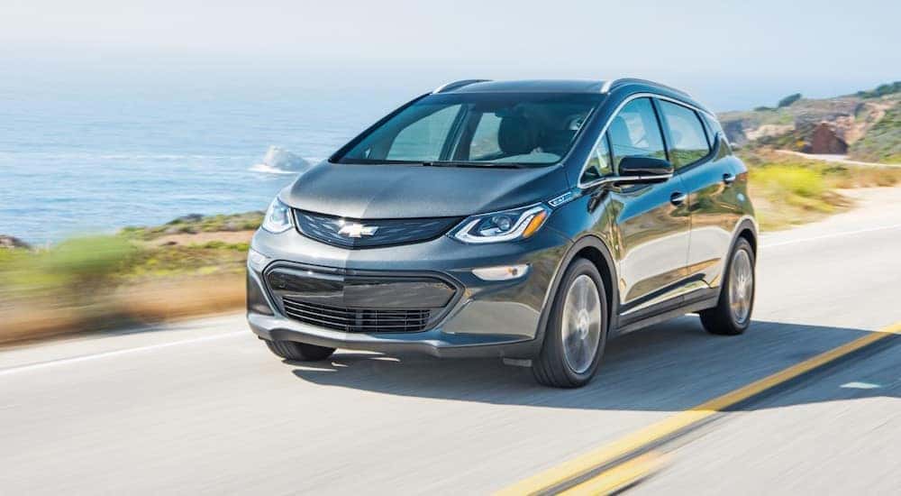 A gray 2019 Chevy Bolt EV is shown driving near an ocean.