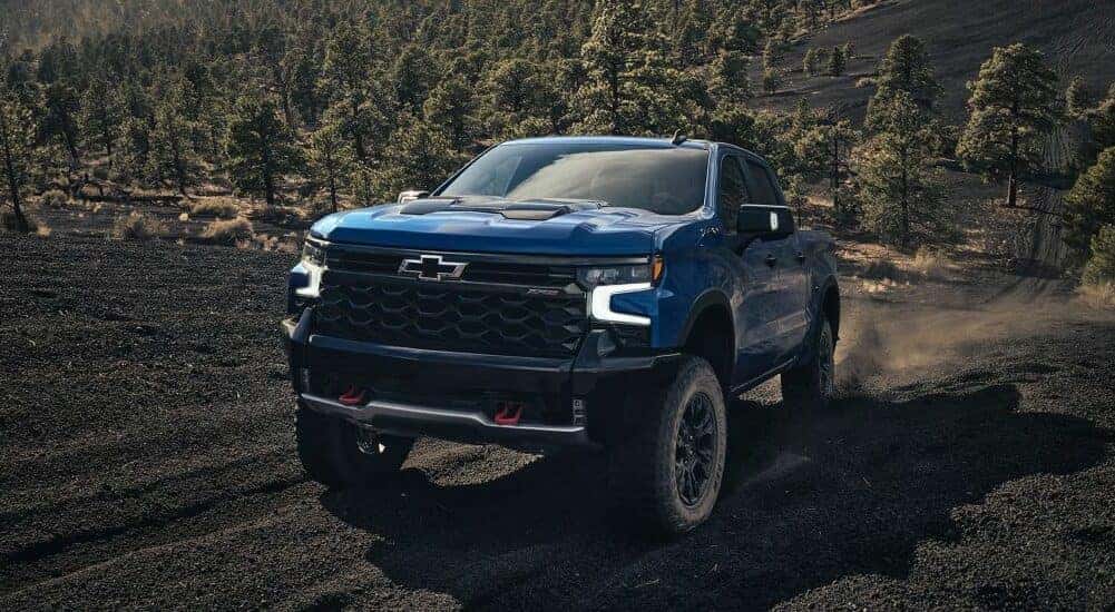A blue 2024 Chevy Silverado 1500 ZR2 driving up a dirt hill.