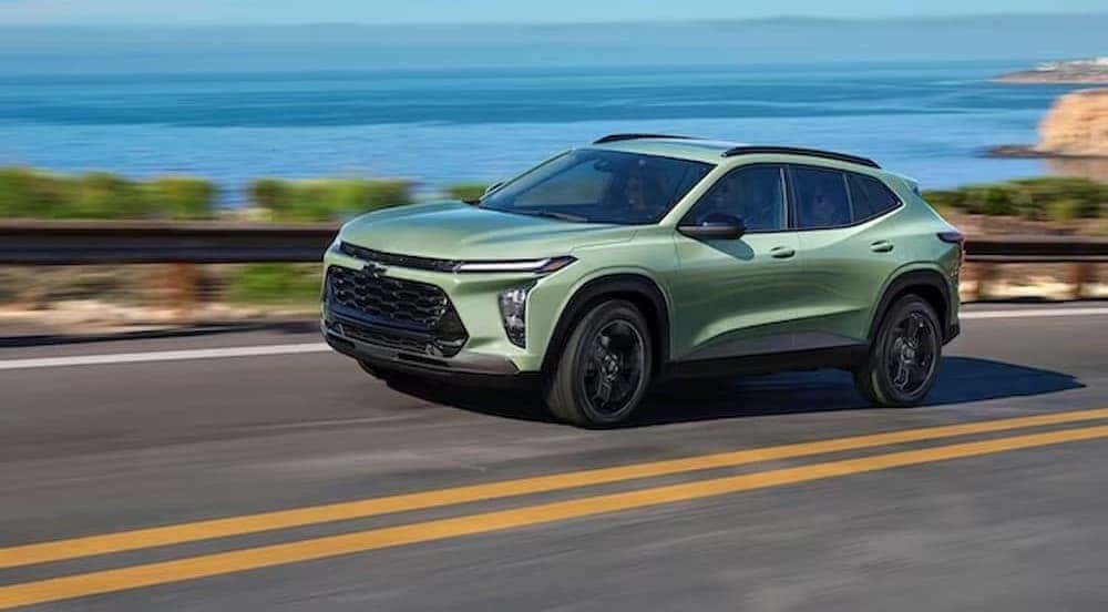 A green 2024 Chevy Trax is shown driving near an ocean.