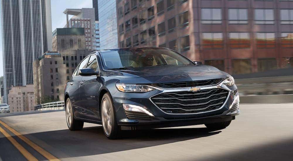 A blue 2020 Chevy Malibu is driving on a city street after leaving a Chevy dealer.