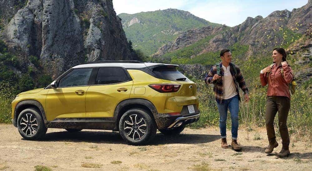 Two hikers walking away from a yellow 2024 Chevy Trailblazer ACTIV parked at a trailhead.