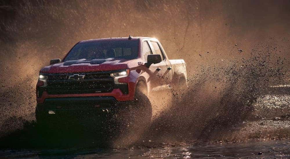 A red 2024 Chevy Silverado 1500 Z71 Trail Boss driving over a muddy road.