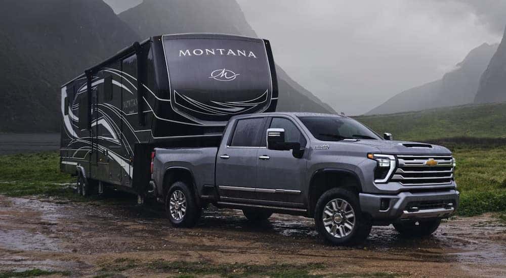A grey 2024 Chevy Silverado 2500 HD towing an RV through a muddy area.