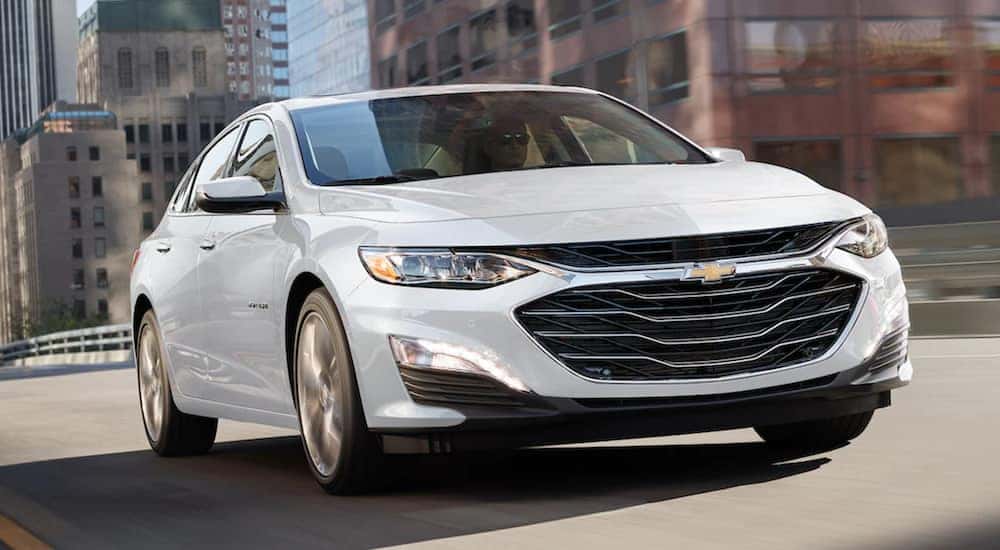 A white 2021 Chevy Malibu is driving through a city after leaving a Kentucky Chevy dealer.