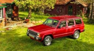 A red 1987 Jeep Cherokee XJ is shown from a high angled parked on grass.