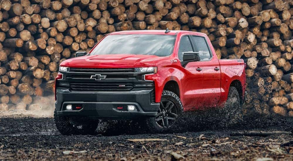 A red 2021 Chevy Silverado 15000 LT Trail Boss is driving in front of a logging pile.