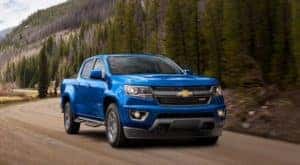 A blue 2020 Chevy Colorado Z71 is shown from the front driving on a tree-lined road.