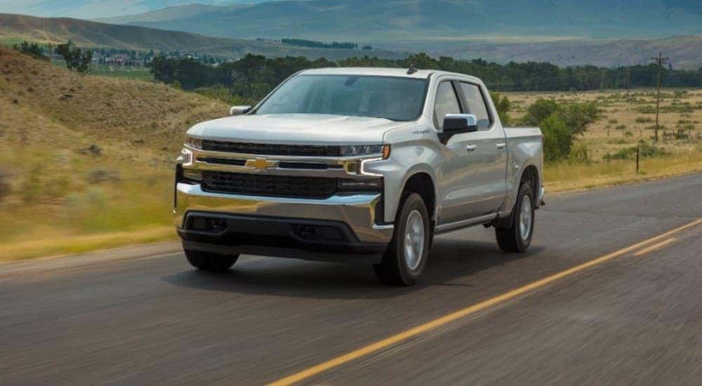 A silver 2020 Chevy Silverado 1500 LT, popular among new vehicles for sale, is driving past rolling hills in Lexington, KY.