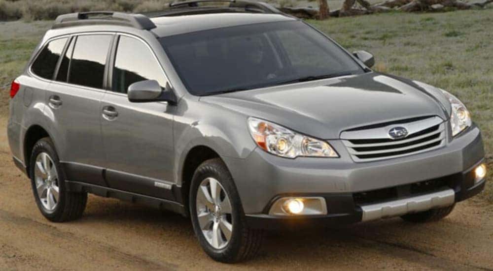 A grey 2010 Subaru Outback is driving on a dirt road.