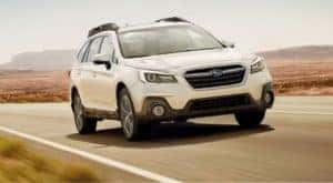 A white 2019 Subaru Outback is shown from the front driving on an open road.
