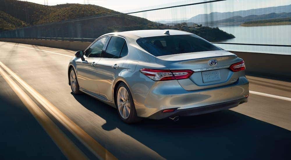 A silver 2020 Toyota Camry XLE Hybrid is shown from the rear driving on an open highway.