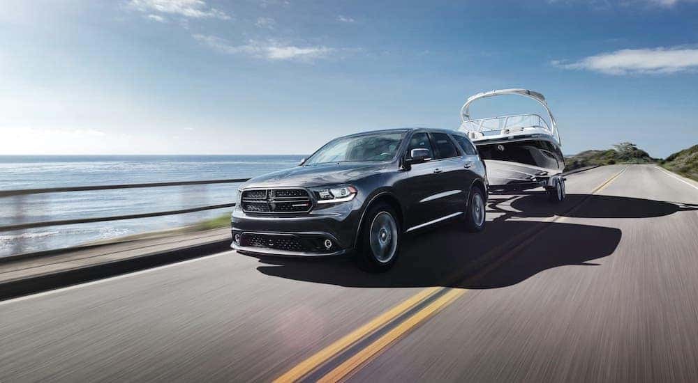 An SUV you might find at a used car dealer near you, a black 2019 Dodge Durango, is shown here towing a boat on a coastal highway.