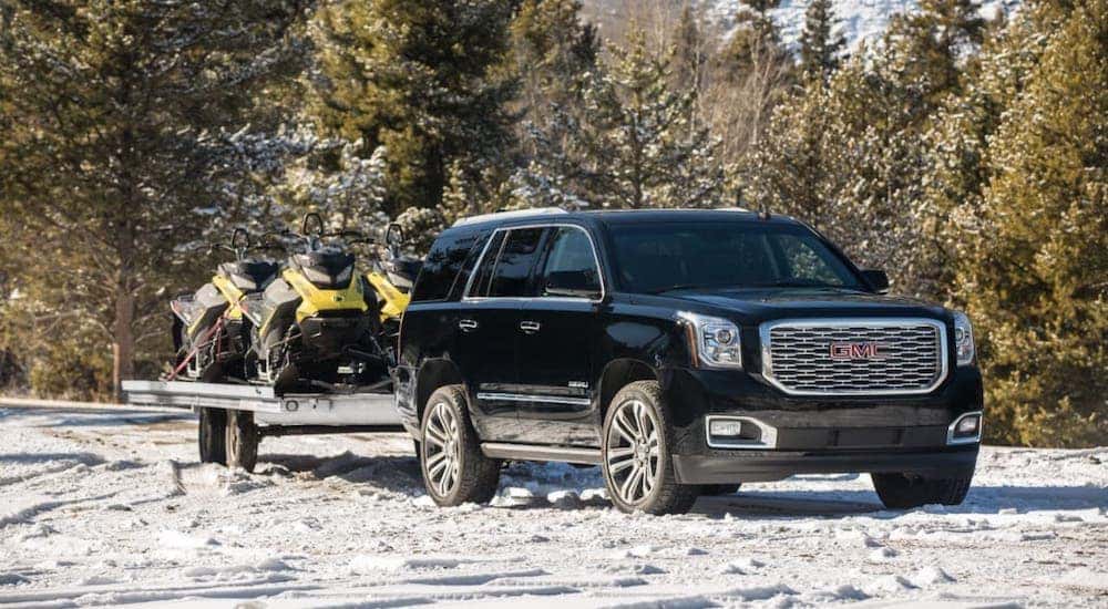 A black 2019 GMC Yukon Denali is towing snowmobiles on a snowy road.