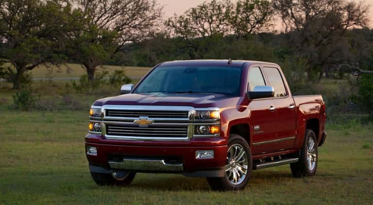 A red 2014 Chevy Silverado High Country, a popular used Chevy Silverado 1500 for sale, is shown parked on grass.