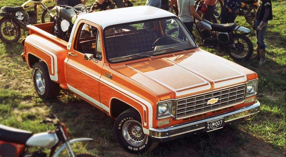 A classic used Chevy truck near me, an orange 1976 Chevy C10 Stepside, is shown from a high angle with multiple dirt bikes parked around it.