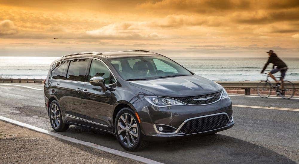 A gray 2017 Chrysler Pacifica is driving in front of a beach after leaving a used minivan dealer.