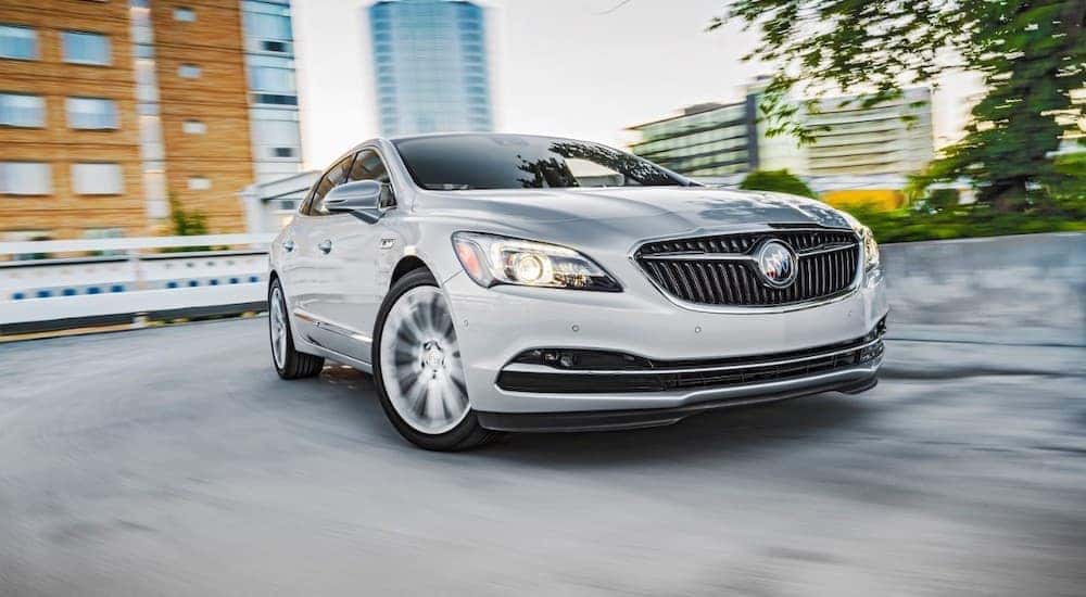 A silver 2017 Buick LaCrosse is driving around a corner past city buildings.