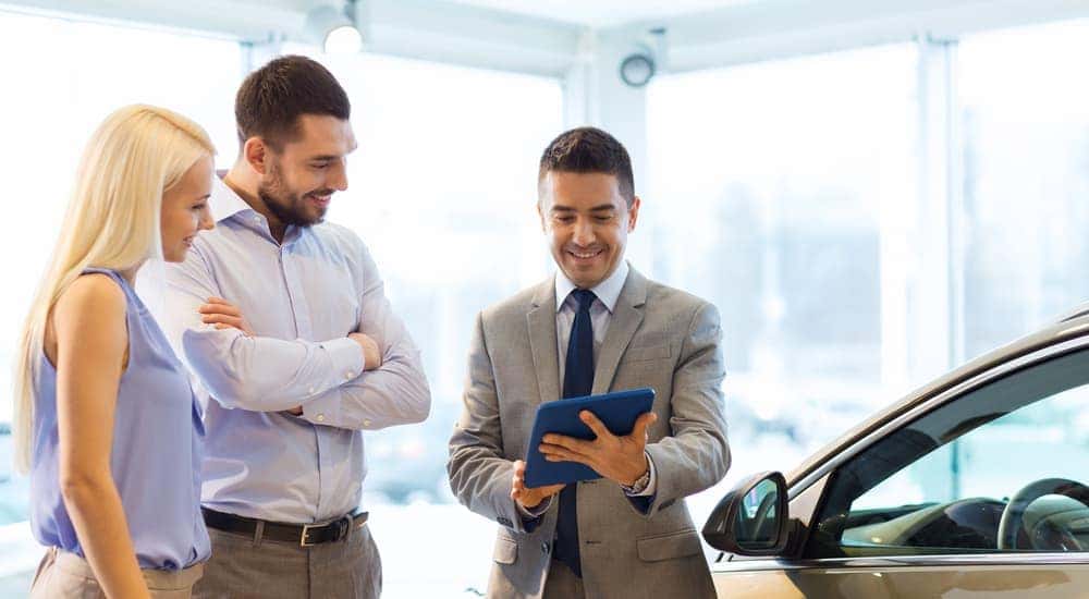 A salesman is talking to a couple about used vehicles for sale in a dealership.