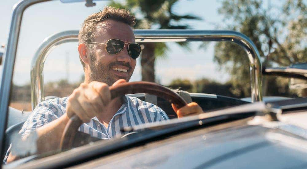 A man is smiling driving his new luxury car after he saw a sign for used luxury vehicles for sale.
