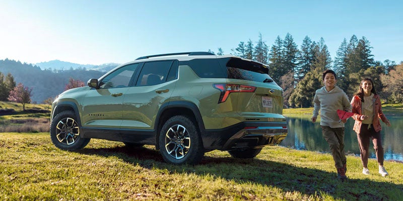 Chevrolet Equinox parked on a grassy field next to a river as two children run past the vehicle
